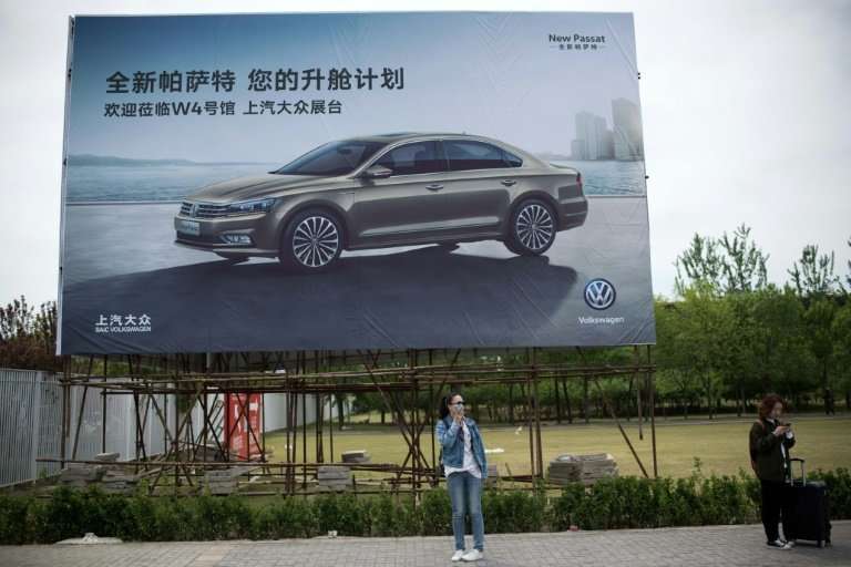 People stand under a billboard advertising a Volkswagen car on the eve of the Beijing Auto Show in Beijing