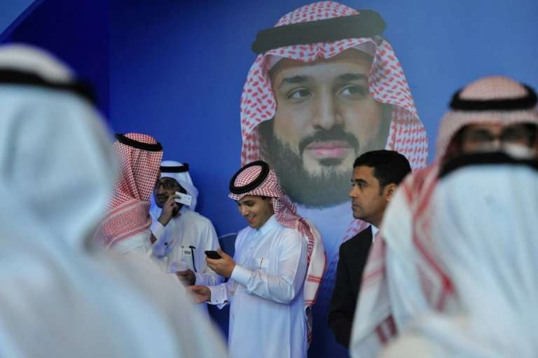 Saudi men chat in front of a poster of Saudi Crown Prince Mohammed bin Salman during the 2017 &quot;MiSK Global Forum,&quot; par