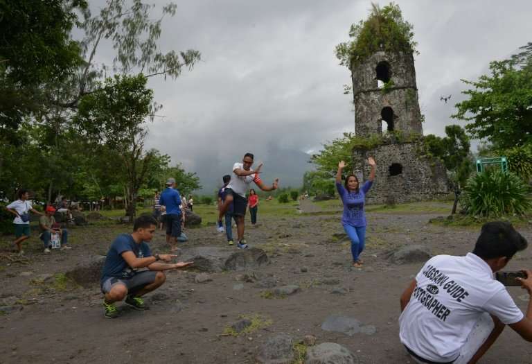 Tourists pose for photos at the old church belfry of Cagsawa town, which juts out of the grass more than two centuries after May