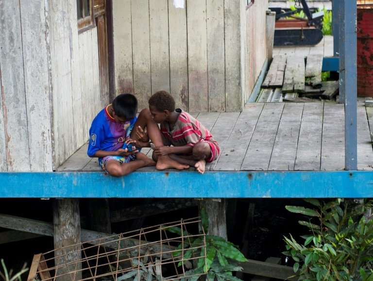 Two Papuan boys play with a phone in Agats, Asmat district, in West Papua, where a few nurses are struggling to treat more than 