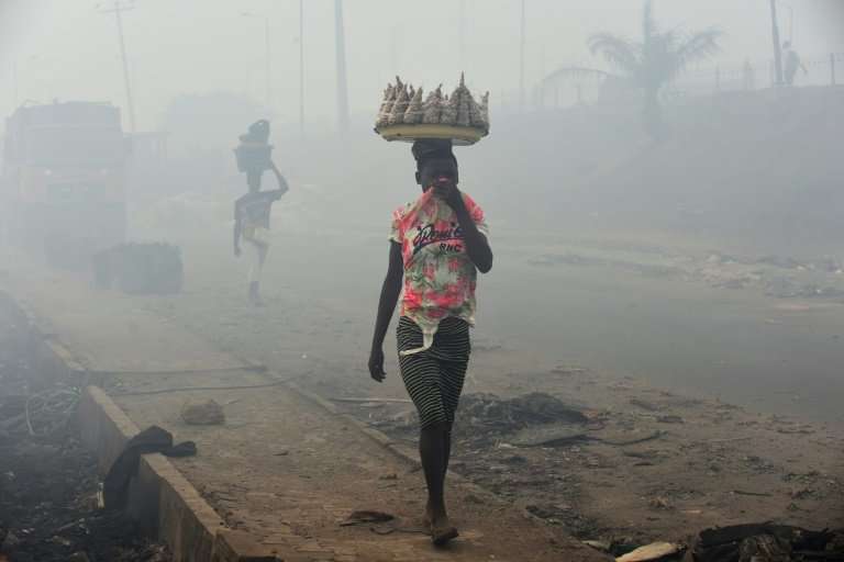 Vendors cover their nose as they walk through smoke emanating from the Olusosun dump site in Lagos, Nigeria's commercial capital