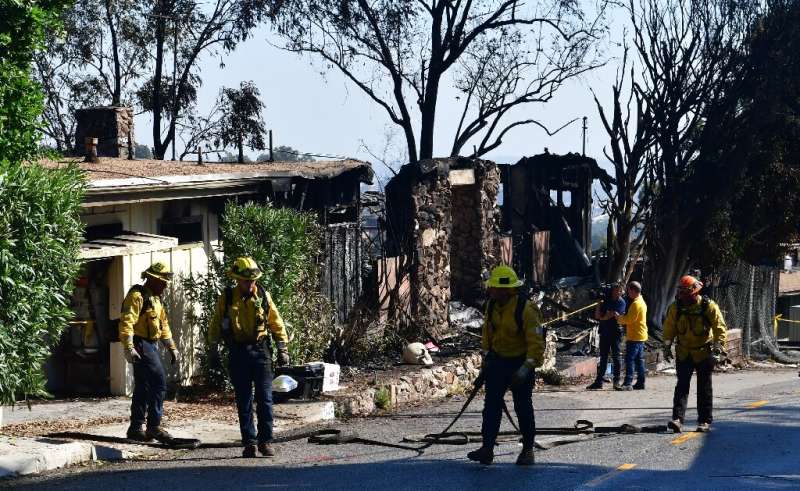 Firefighters gather their hoses near destroyed homes along North Tigertail Road near the Getty Center in Los Angeles on October 