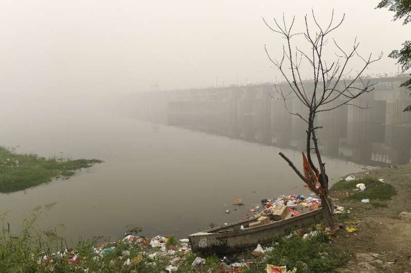 A boat is seen amidst heavy smog conditions surrounded by rubbish near a bridge along the Yamuna River in New Delhi