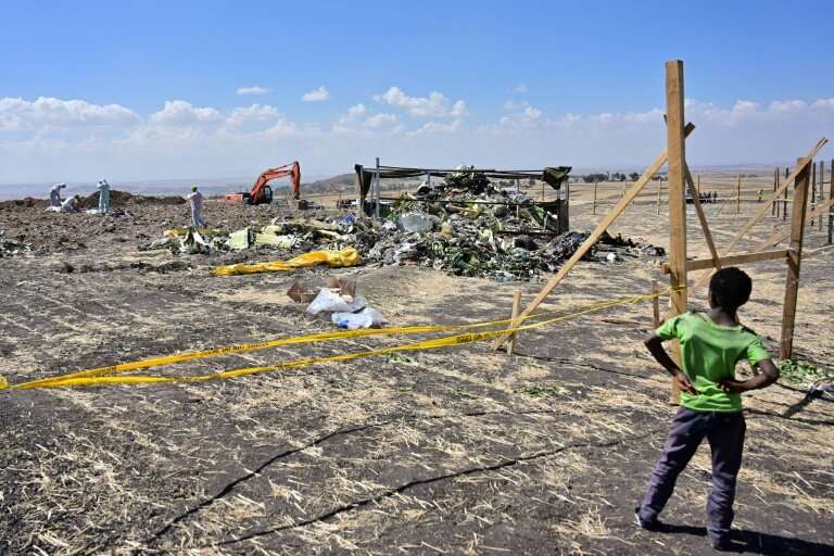 A boy looks on as forensic investigators work at the crash site of an Ethiopian Airlines Boeing 737 MAX aircraft