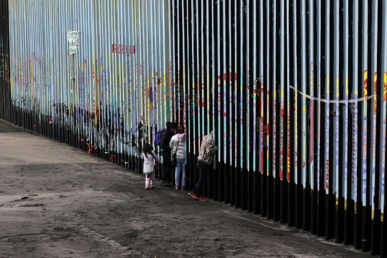 A family of Central American migrants look through the US-Mexico border fence in Baja California state, Mexico