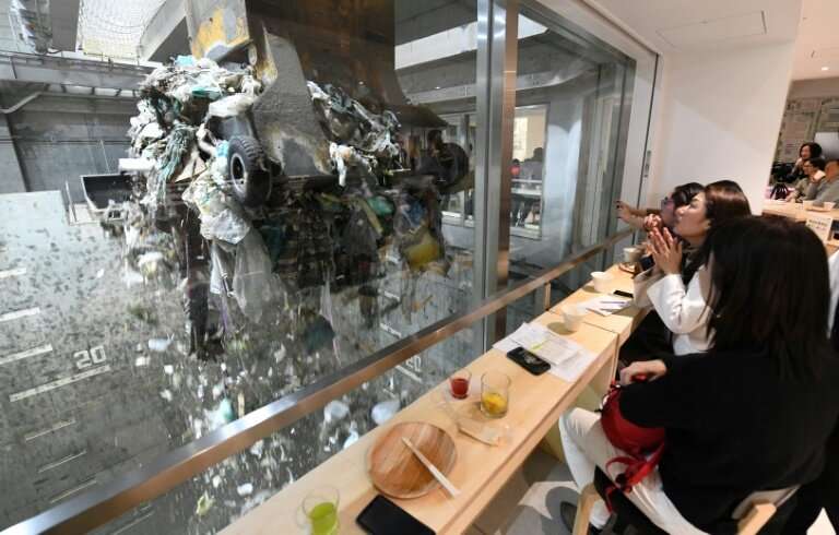A group of young Japanese enjoy food and drinks while watching an enormous crane pick up trash for incineration at a combustible
