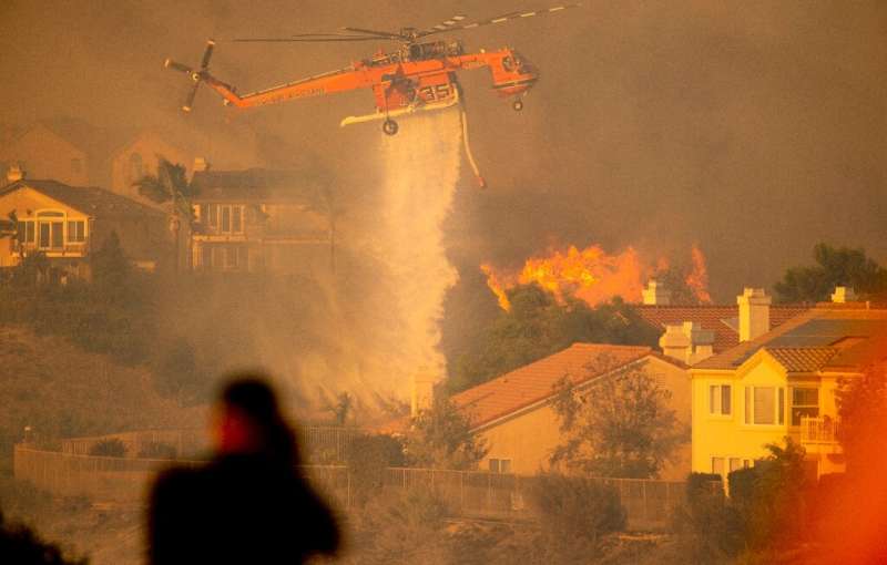 A helicopter drops water to help fight flames as the Saddleridge Fire in the Porter Ranch section of Los Angeles, California on 