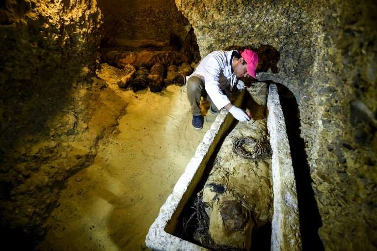 An archaeologist brushes a newly-discovered mummy laid inside a sarcophagus, part of a collection found in burial chambers datin