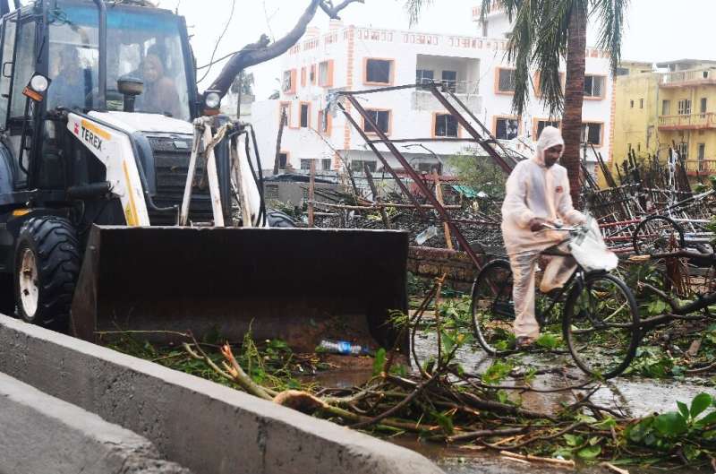 An Indian resident rides a bike past a bulldozer clearing debris from a road in Puri