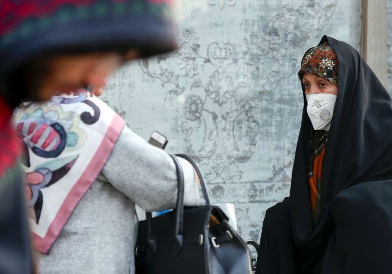 An Iranian woman wearing a breathing mask walks down a street as a blanket of smog covers Tehran