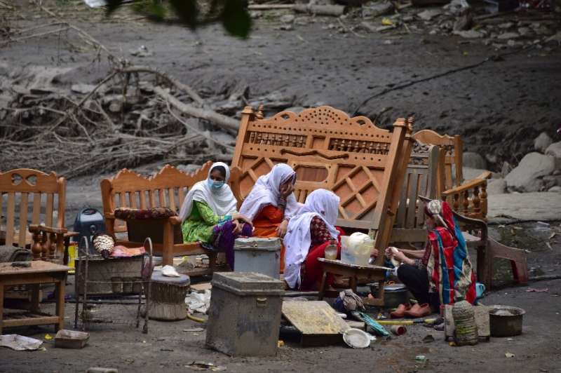 A Pakistani Kashmiri family gather around their belongings outside their damaged house following heavy monsoon rains in Neelum v