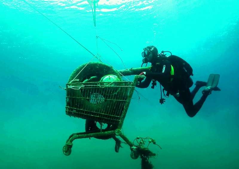 A volunteer for Greek environmental group Aegean Rebreath collects a trash-filled shopping cart from the sea on the Ionian islan