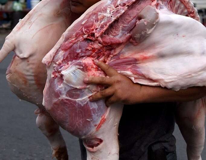 A worker carries pig carcasses at a market in Phnom Penh