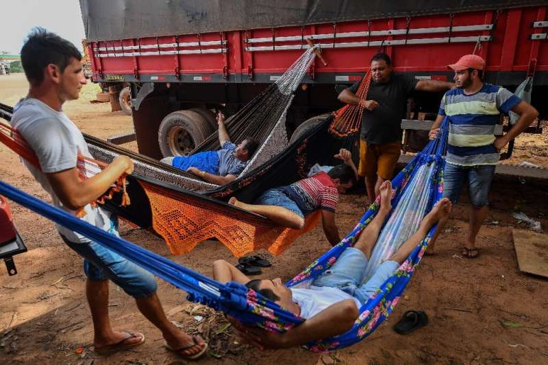 Brazilian trucker Erik Fransuer (L) speaks with other drivers resting on hammocks at a gas station in Ruropolis—he spends at lea
