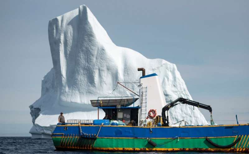 Edward Kean stands on his boat in front of an iceberg in Bonavista Bay, Newfoundland—he trades in iceberg water