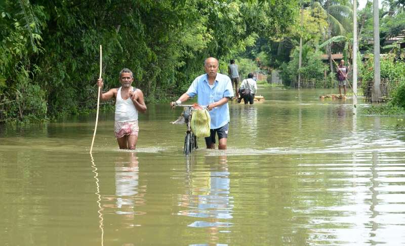 Indian men walk in flood waters in Kamrup districts of Assam, which has been badly hit by monsoon rains