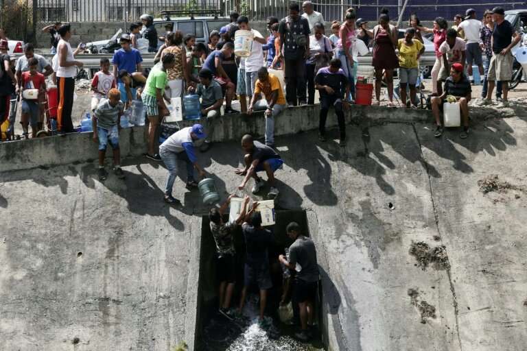 People collect water from a broken pipe flowing into a sewage canal at the Guaire river in Caracas on March 11, 2019