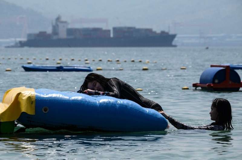 People swim at a beach in Subic Bay where a container ship hired by Canada is loaded with trash that the Philippines has ordered