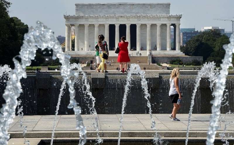 People walk near the World War II Memorial on the National Mall with the Lincoln Memorial in the background as temperatures soar