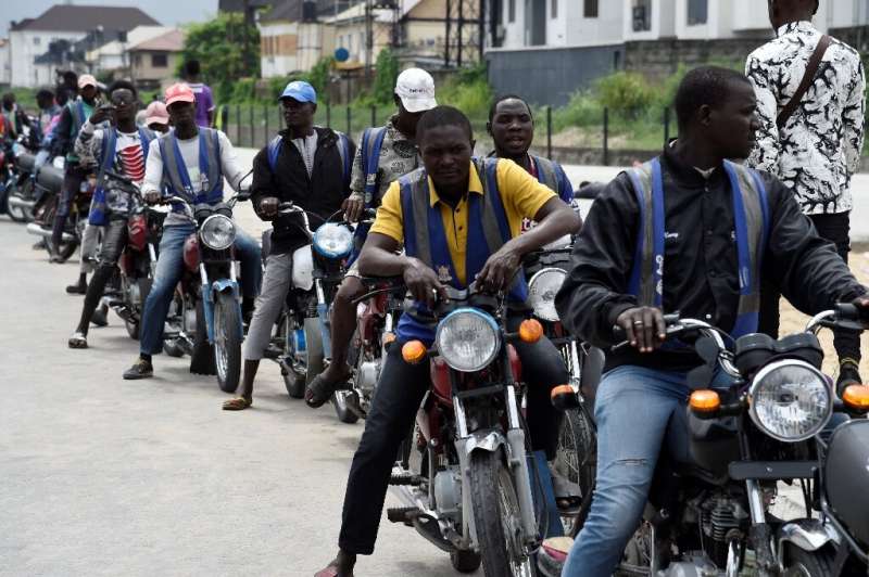 Regular motorcycle taxis queue for custom in Lagos—helmets and safety kits are absent, and passengers have to haggle over fares