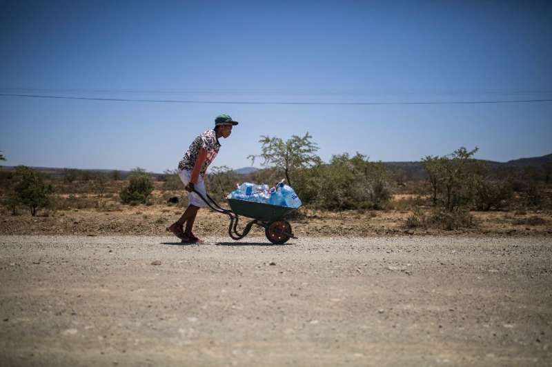 The hot way home: A young man pushes a wheelbarrow with bottles filled with water