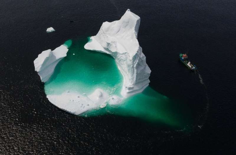 This aerial photo shows Edward Kean's boat passing an iceberg in Bonavista Bay—it's a difficult task to break up and &quot;harve
