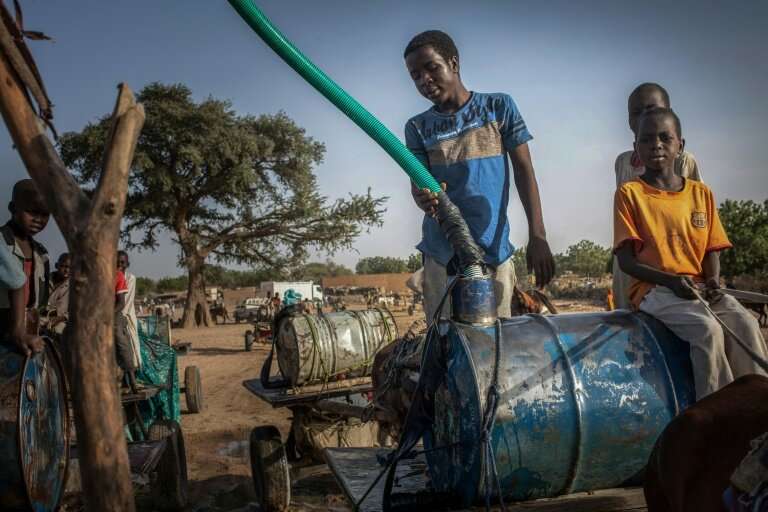 Young hawkers fill barils with water in the Moura wadi in Hadjer Hadid