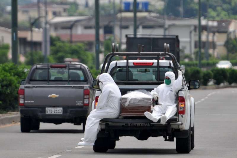 People wearing protective suits sit next to a coffin on a truck near Los Ceibos hospital in Guayaquil, Ecuador