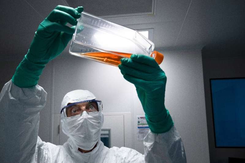 A lab technician in Personal Protective Equipment (PPE) looks at a reagent bottle before performing vaccine tests at French phar
