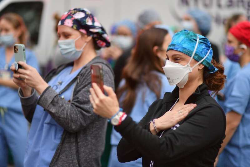 Healthcare workers take video as people cheer to show their gratitude to medical staff outside NYU Langone Health hospital on Ap