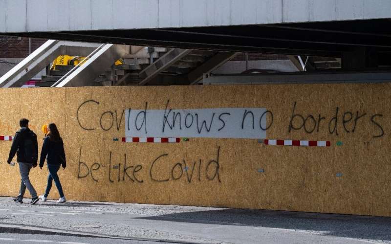 People walk past a graffito reading: &quot;Covid(19) knows no borders, be like Covid&quot; in Berlin