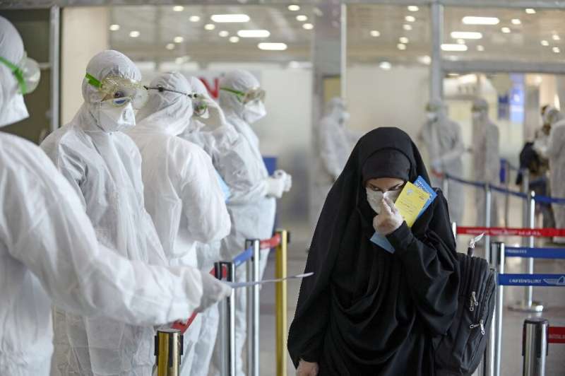 Medical staff distribute information sheets to Iraqi passengers returning from Iran at Najaf International Airport