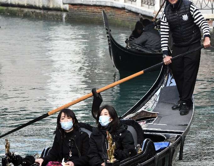 A gondolier steers tourists in facemasks along a canal in Venice