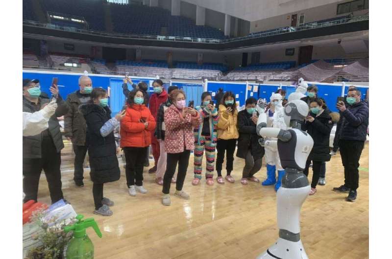 A handhout picture provided by CloudMinds shows Wuhan smart field hospital staff looking at an XR1 robot being deployed for coro