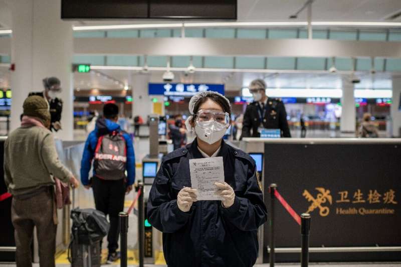 A health quarantine officer (C), wearing protective gear at Daxing International Airport in Beijing, holds a health document to 