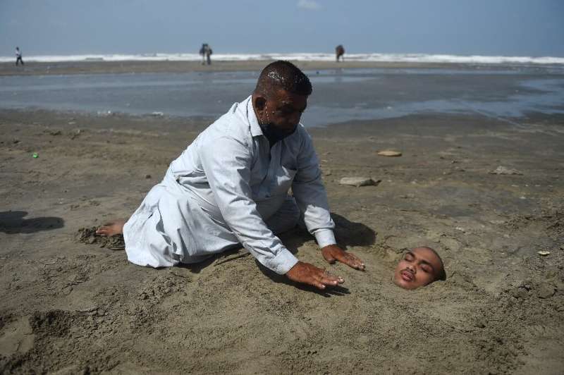 A man buries his paralysed son in sand on a beach in Karachi during the eclipse. Folklore has it if the eclipse passes over them