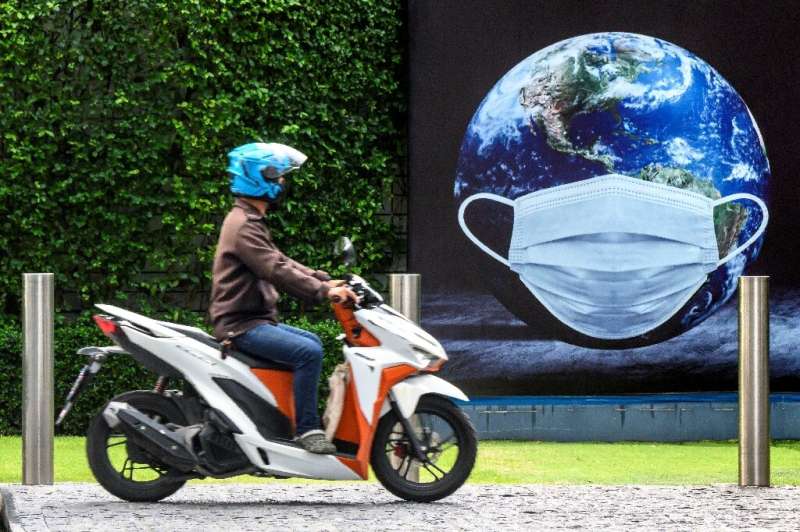 A man rides his scooter in front of a COVID-19 coronavirus related poster  in Bangkok