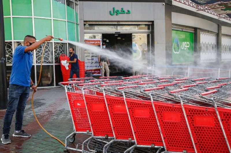 A mask-clad Palestinian worker disinfects supermarket carts
