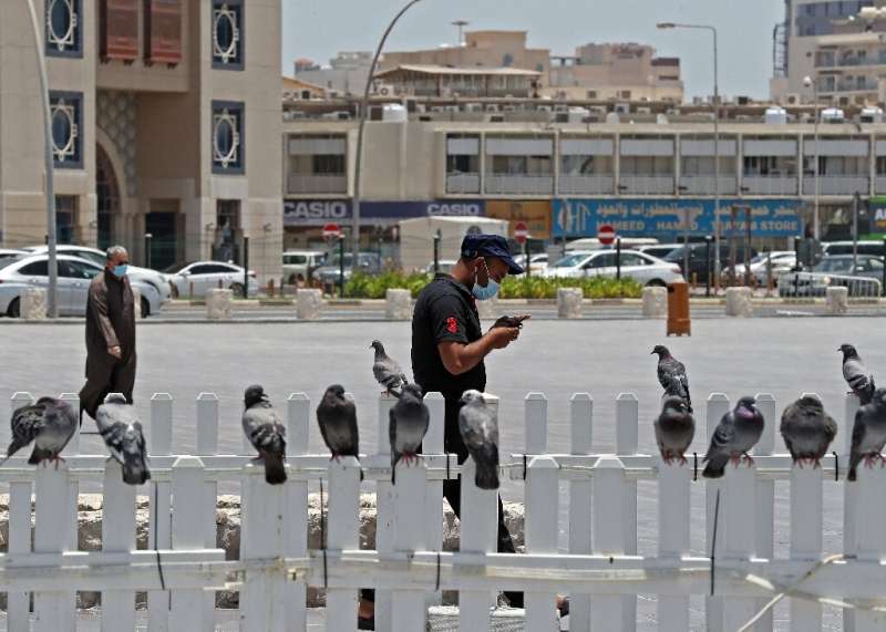 A masked man checks his phone in Qatar where residents and citizens have been required by law to install a coronavirus contact t