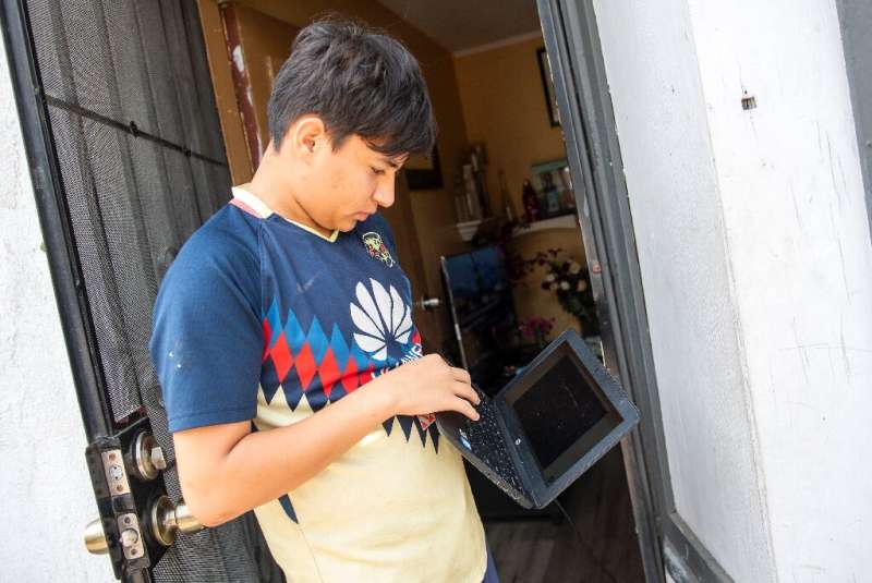 Angel, 13, stands outside  his home trying to connect his computer to the wifi hotspot provided by a parked van from JFK company