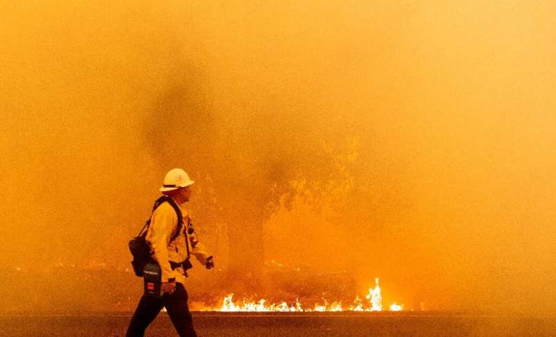 A Pacific Gas and Electric firefighter walks down a road as flames approach in Fairfield, California during the LNU Lightning Co