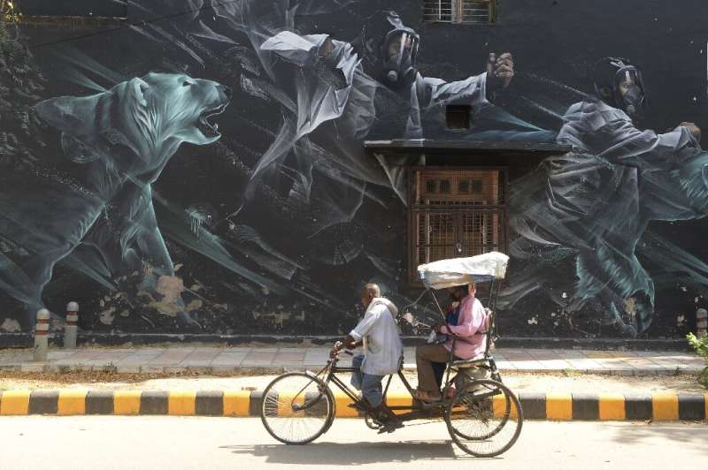 A rickshaw driver carries passengers  past a mural in the Lodhi Art District in New Delhi