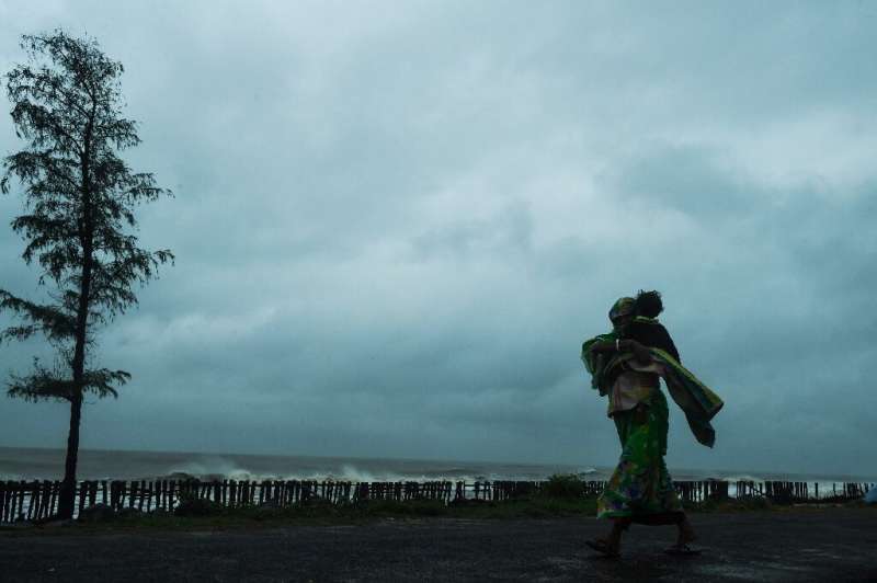 A woman carries her child as she walks along a road near the Tajpur Beach to take shelter ahead of the expected landfall of Cycl