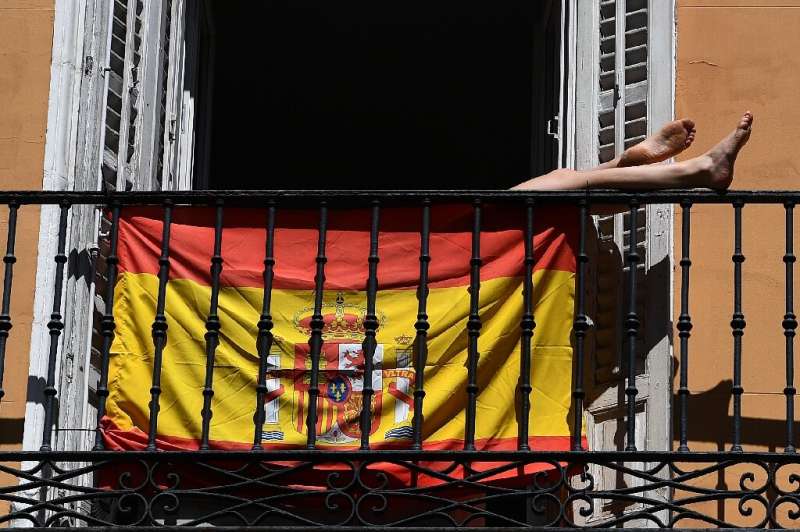 A woman sunbathes behind a Spanish flag on her balcony in Madrid during the national lockdown