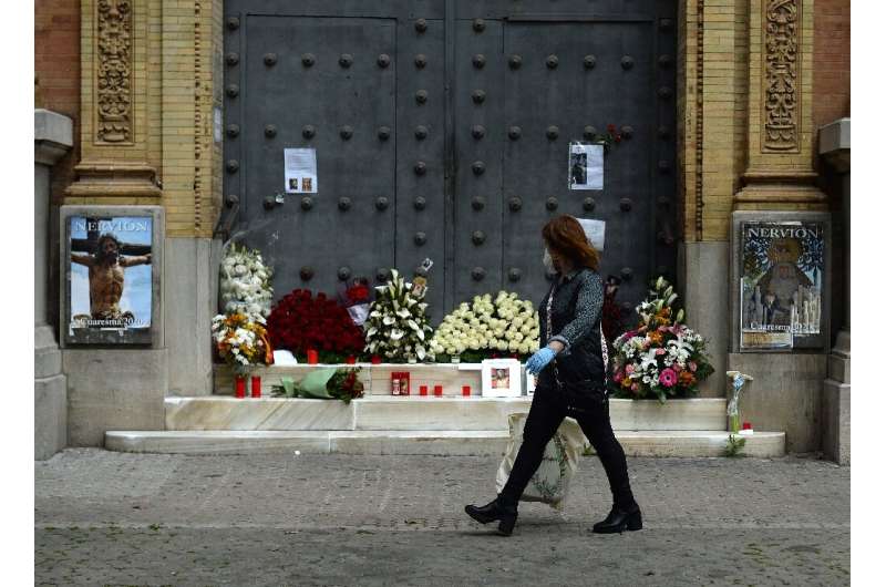 A woman walks past a church in Seville, adorned with flowers and candles left by the faithful after Easter processions were canc