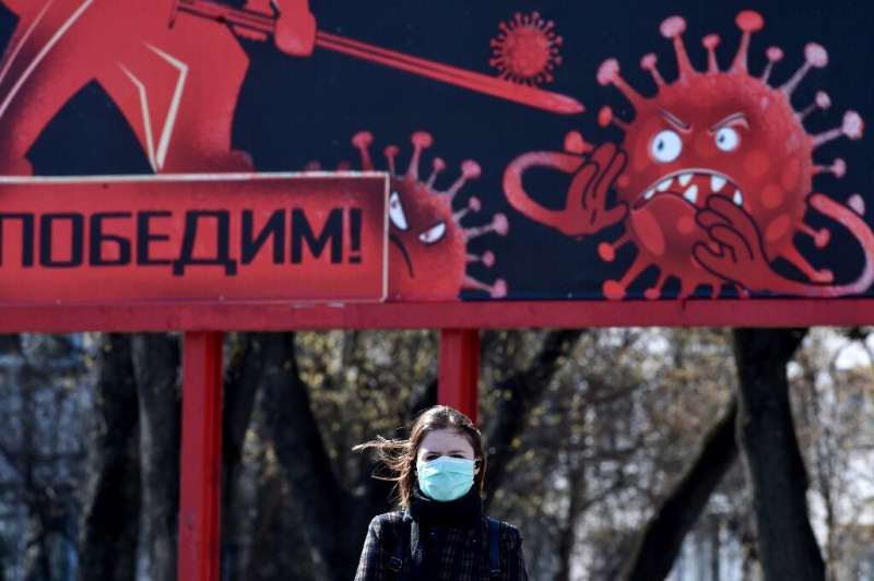 A woman wearing a face mask walks past a sign depicting a virus in Minsk