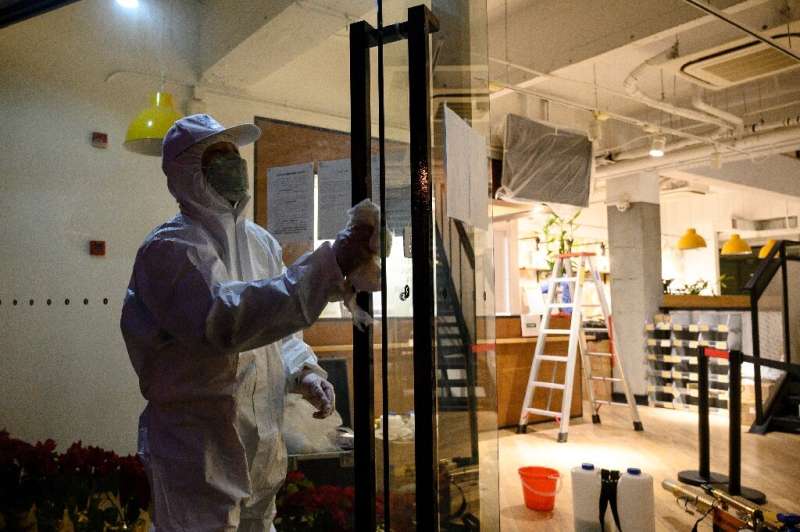 A worker wearing a protective suit disinfects door handles of a business establishment in Shanghai