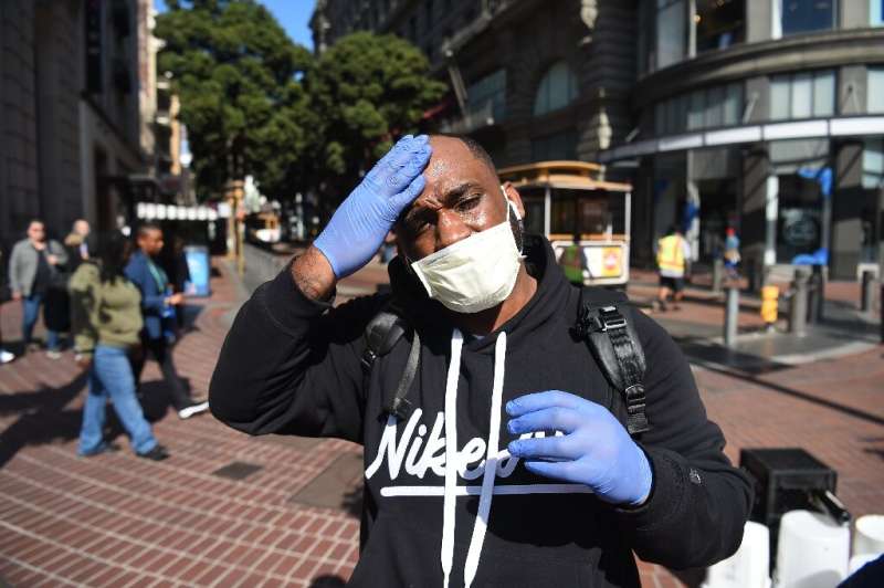 Cameron Nightingale, trying to protect himself from the new coronavirus, adjusts his mask and gloves in San Francisco, after off