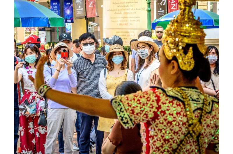 Chinese tourists wearing face masks watch a traditional Thai dance at Erawan shrine, a popular landmark in Bangkok