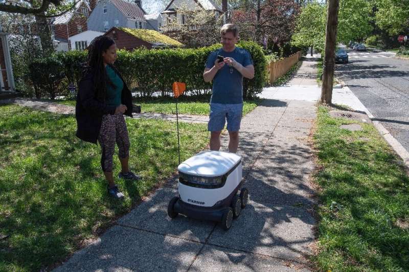 Kimmo Kartano uses his smartphone to open a food delivery robot from the Broad Branch Market grocery store as Audra Grant looks 